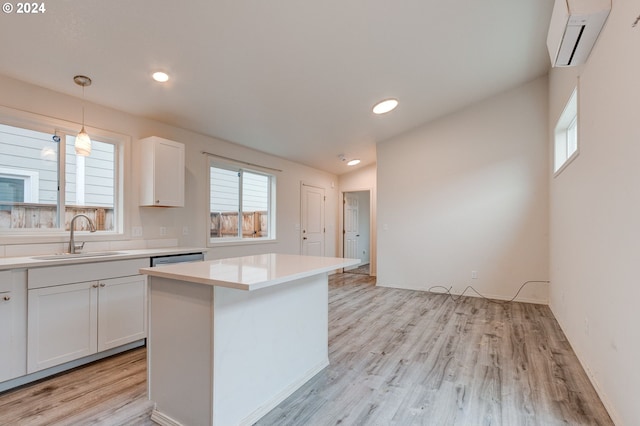 kitchen featuring white cabinetry, sink, hanging light fixtures, light hardwood / wood-style flooring, and a wall mounted AC