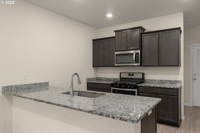 59 NE 134th Pl, Portland, OR 97230 - kitchen featuring appliances with stainless steel finishes, a sink, dark brown cabinets, light wood-style flooring, and a peninsula