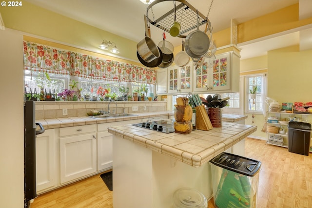 kitchen with tile countertops, sink, white cabinetry, black electric stovetop, and light wood-type flooring