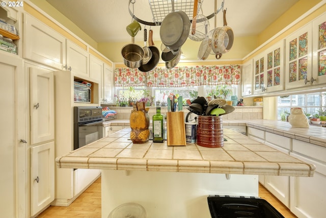 kitchen with tile counters, wall oven, light wood-type flooring, and white cabinets