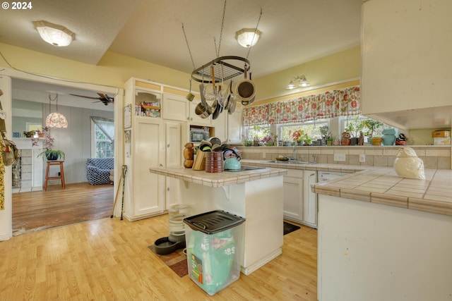 kitchen with tile counters, sink, white cabinetry, and light hardwood / wood-style floors