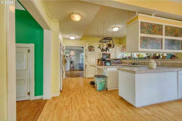 kitchen with white cabinets, tile countertops, kitchen peninsula, and light hardwood / wood-style flooring