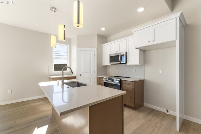 kitchen featuring a center island with sink, decorative light fixtures, stainless steel appliances, white cabinetry, and a sink