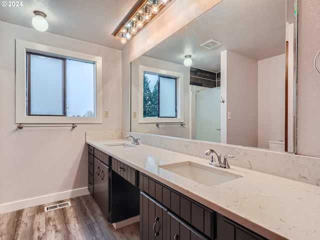 bathroom featuring dual sinks, toilet, hardwood / wood-style floors, a textured ceiling, and large vanity