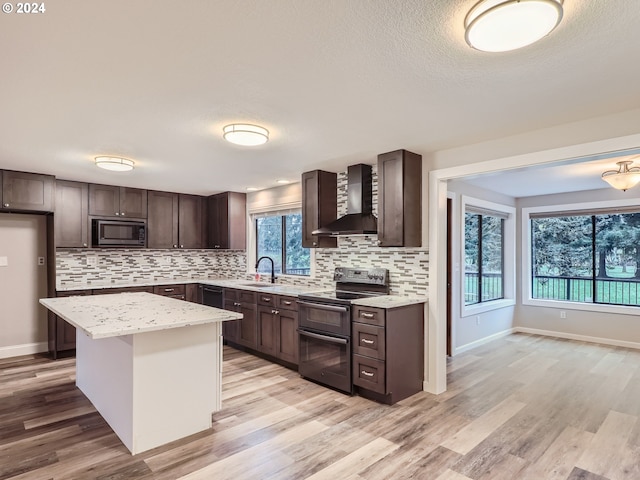 kitchen with light hardwood / wood-style floors, plenty of natural light, wall chimney exhaust hood, and black appliances