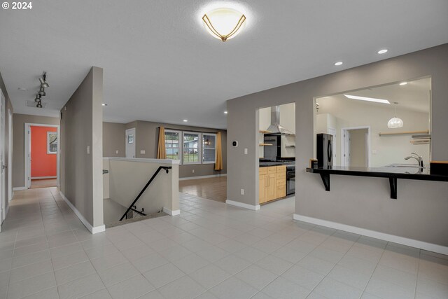 kitchen with vaulted ceiling, black fridge, a kitchen bar, wall chimney exhaust hood, and sink