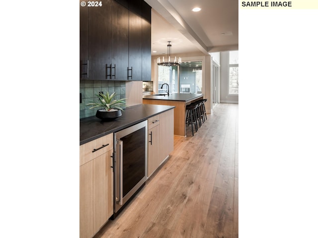 kitchen with hanging light fixtures, sink, beverage cooler, light hardwood / wood-style floors, and decorative backsplash