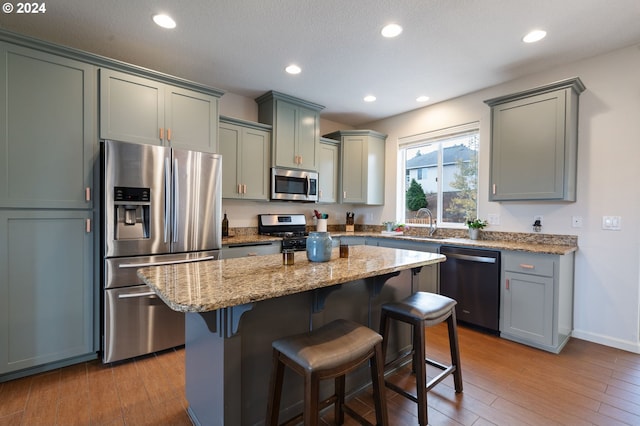 kitchen with appliances with stainless steel finishes, light stone countertops, a kitchen bar, light wood-type flooring, and a center island