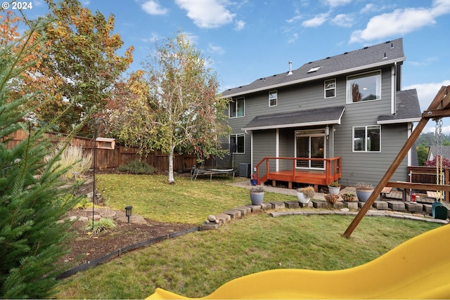 rear view of house featuring a patio, a wooden deck, a trampoline, and a lawn