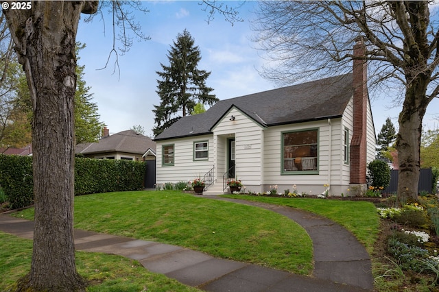 view of front of property with a front yard, roof with shingles, fence, and a chimney