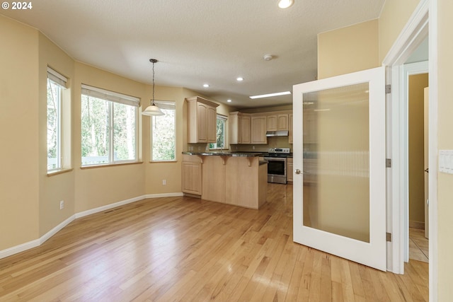 kitchen featuring light wood-type flooring, electric range, a kitchen bar, light brown cabinets, and decorative light fixtures