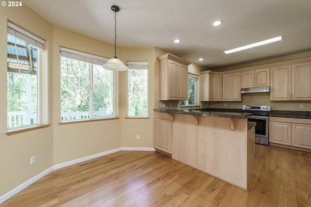 kitchen featuring stainless steel range with electric cooktop, light brown cabinets, decorative light fixtures, and light hardwood / wood-style floors