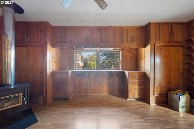 interior space with wooden walls, a wood stove, ceiling fan, and light hardwood / wood-style flooring