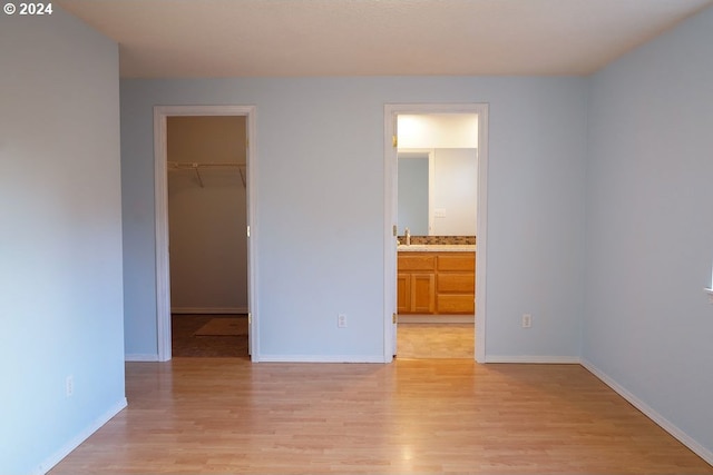 unfurnished bedroom featuring a closet, light hardwood / wood-style floors, ensuite bath, and a walk in closet