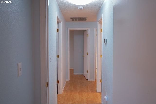 hallway with a textured ceiling and light wood-type flooring