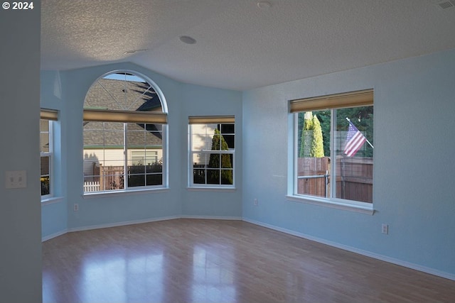 spare room with hardwood / wood-style floors, vaulted ceiling, and a textured ceiling