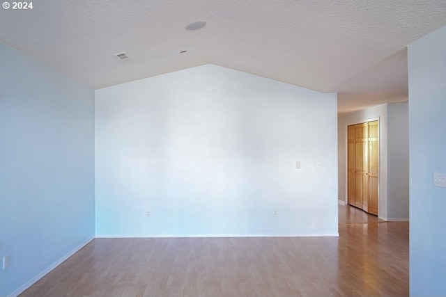 spare room featuring light hardwood / wood-style floors, a textured ceiling, and lofted ceiling