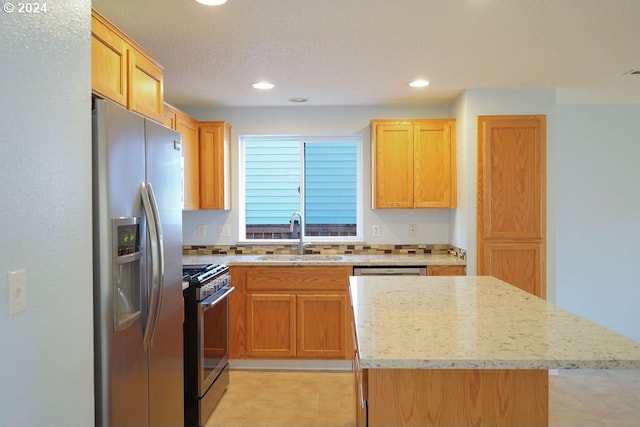 kitchen featuring appliances with stainless steel finishes, sink, light stone counters, and a kitchen island