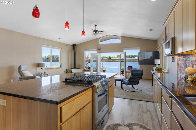 kitchen featuring appliances with stainless steel finishes, decorative light fixtures, a kitchen island, light wood-type flooring, and vaulted ceiling