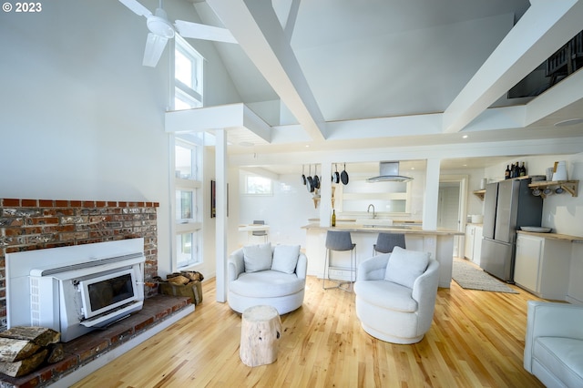 living room with a towering ceiling, light wood-type flooring, ceiling fan, sink, and beam ceiling