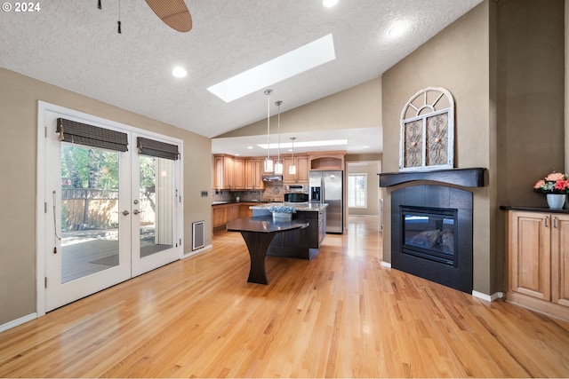 kitchen featuring ceiling fan, hanging light fixtures, stainless steel fridge, a kitchen bar, and a kitchen island