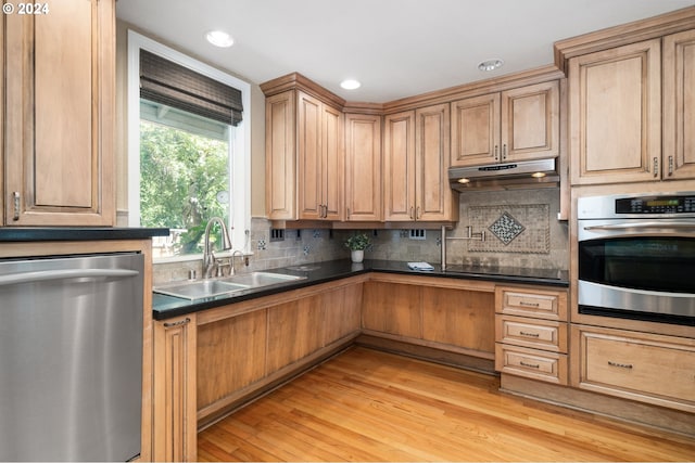 kitchen with tasteful backsplash, sink, stainless steel appliances, and light hardwood / wood-style floors