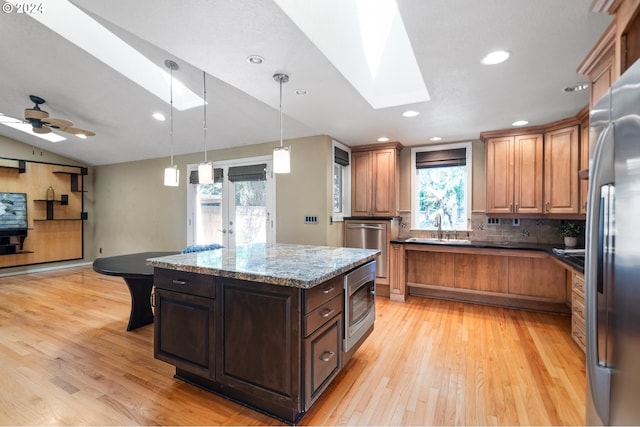 kitchen with appliances with stainless steel finishes, light wood-type flooring, backsplash, vaulted ceiling with skylight, and a kitchen island