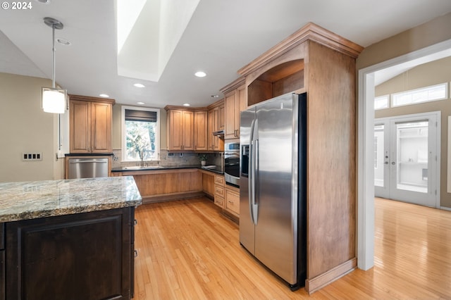 kitchen featuring pendant lighting, decorative backsplash, appliances with stainless steel finishes, stone countertops, and light hardwood / wood-style floors