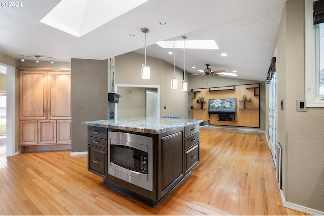 kitchen featuring stainless steel microwave, ceiling fan, decorative light fixtures, a kitchen island, and dark brown cabinetry