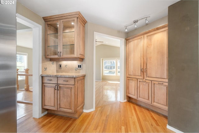 interior space with vaulted ceiling, stainless steel fridge, light stone countertops, tasteful backsplash, and light hardwood / wood-style floors