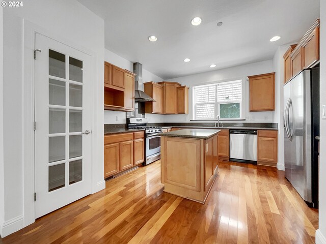 kitchen featuring light wood-type flooring, stainless steel appliances, a center island, and wall chimney exhaust hood