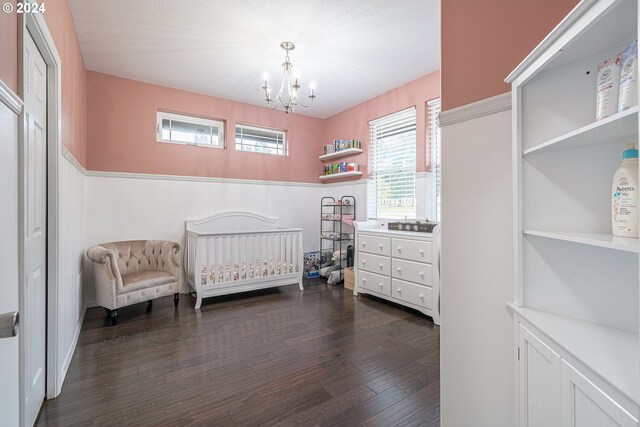 bedroom featuring dark wood-type flooring, a nursery area, and a chandelier