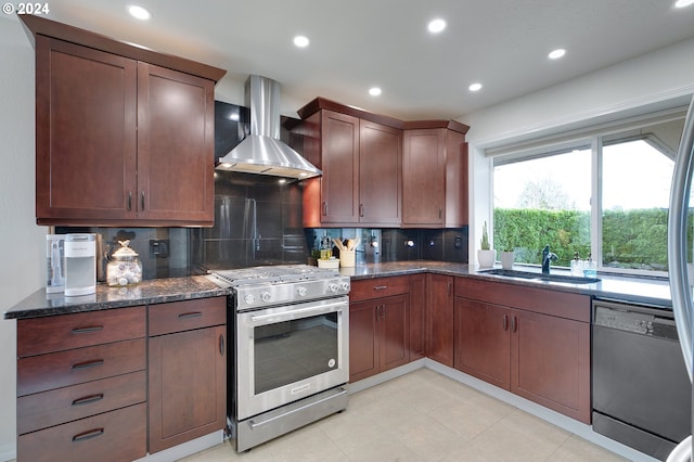 kitchen with wall chimney range hood, decorative backsplash, appliances with stainless steel finishes, dark stone countertops, and sink