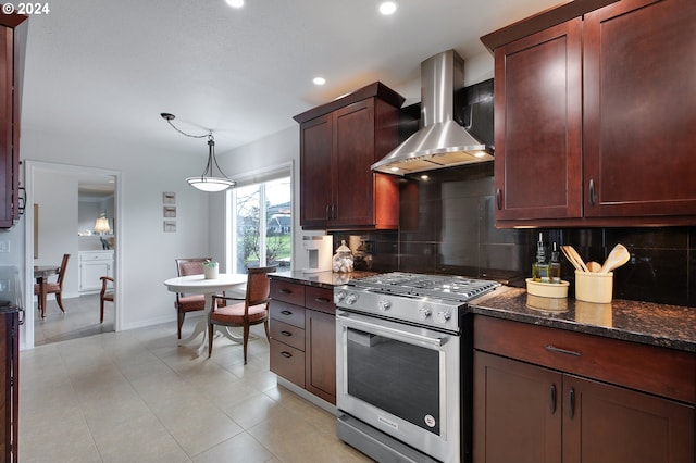 kitchen with wall chimney range hood, decorative backsplash, hanging light fixtures, stainless steel stove, and dark stone countertops