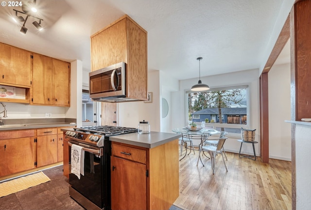 kitchen featuring appliances with stainless steel finishes, dark hardwood / wood-style floors, decorative light fixtures, sink, and stainless steel counters