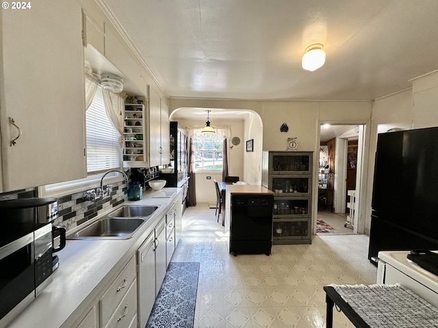 kitchen with black refrigerator, tasteful backsplash, sink, white cabinets, and hanging light fixtures