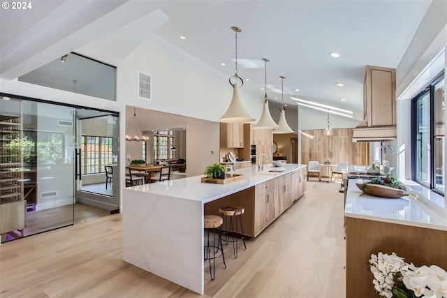 kitchen with pendant lighting, a large island with sink, a kitchen breakfast bar, light brown cabinetry, and light hardwood / wood-style floors