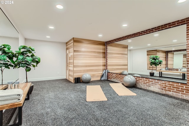 workout room featuring dark carpet and brick wall