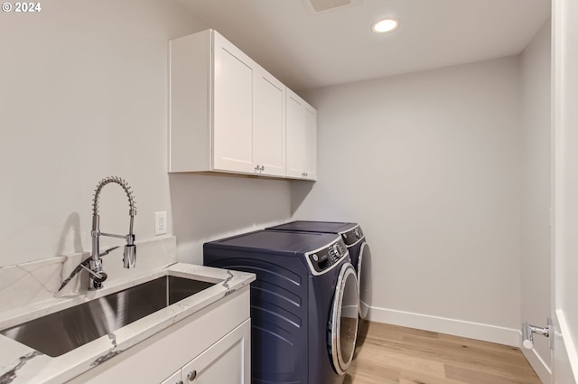 laundry area with cabinets, light wood-type flooring, separate washer and dryer, and sink