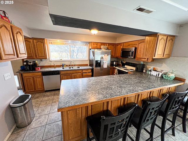 kitchen featuring sink, kitchen peninsula, a kitchen bar, light tile patterned floors, and appliances with stainless steel finishes