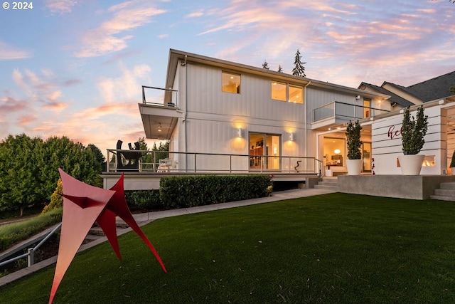 back house at dusk with a balcony and a yard