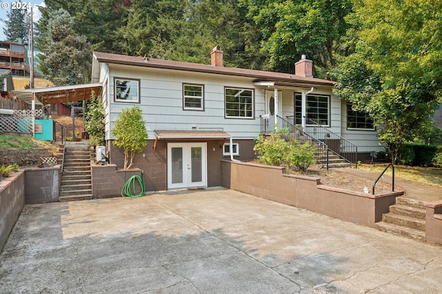 rear view of property with a chimney, driveway, a patio, french doors, and stairs