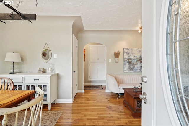 entrance foyer with arched walkways, light wood-style flooring, a textured ceiling, and baseboards