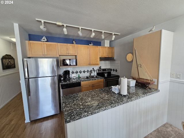 kitchen with appliances with stainless steel finishes, dark stone counters, a textured ceiling, dark hardwood / wood-style floors, and kitchen peninsula