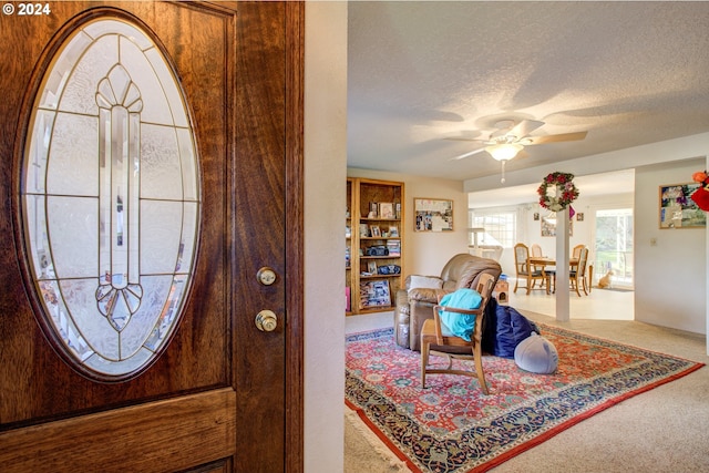 carpeted entryway with ceiling fan and a textured ceiling