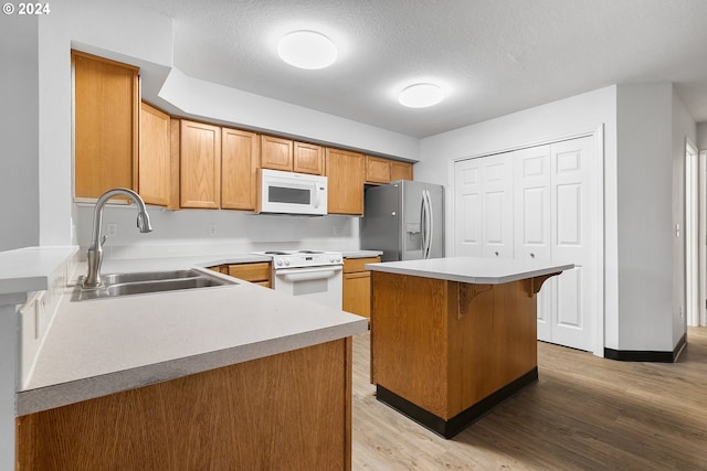 kitchen featuring sink, a center island, a textured ceiling, white appliances, and light wood-type flooring