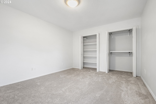 unfurnished bedroom with light colored carpet and multiple closets