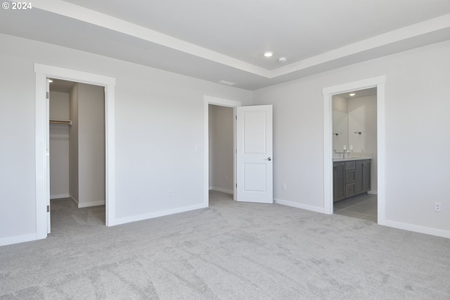 unfurnished bedroom with a spacious closet, a closet, ensuite bathroom, and light colored carpet