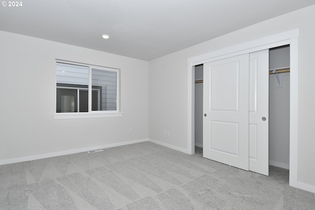 unfurnished bedroom featuring a closet and light colored carpet