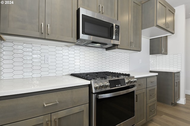 kitchen with light stone countertops, tasteful backsplash, wood-type flooring, and stainless steel appliances